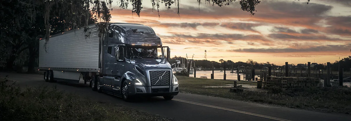 Tractor-trailer traveling past a waterfront at sunset